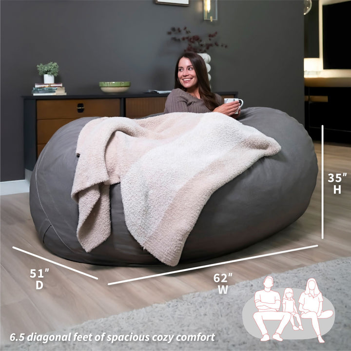 Woman sitting on a large gray bean bag with a blanket, surrounded by room dimensions and usage illustrations. #color_fog-brushed-denim