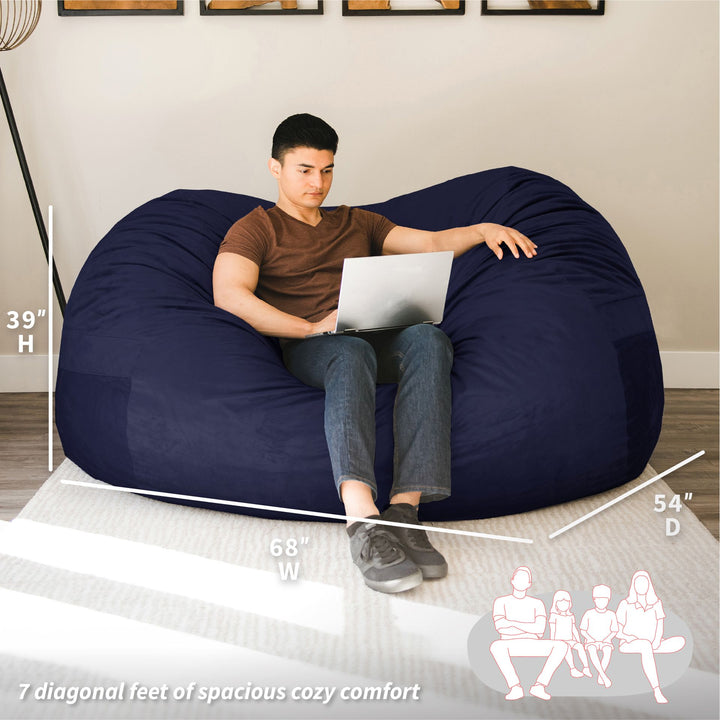 Man sitting on a large navy bean bag with laptop, surrounded by measurements and illustrations. #color_midnight-plush