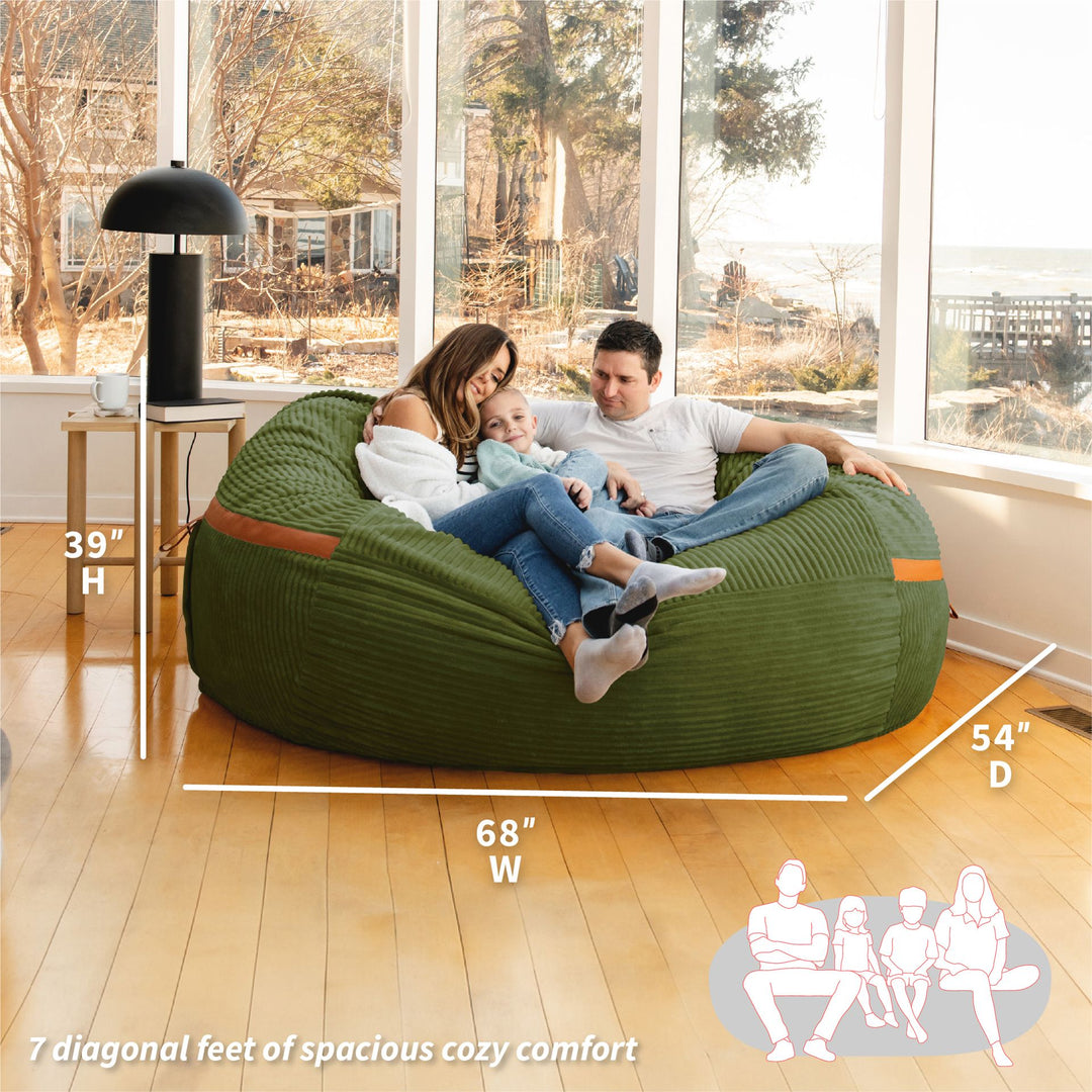 Family sitting on a large green bean bag with dimensions displayed #color_moss-green-corded-plush