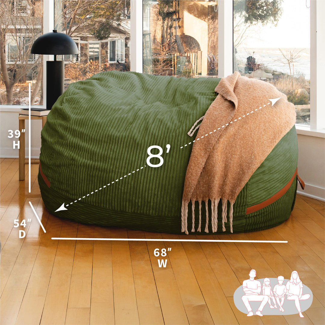 Green bean bag chair with measurements and a blanket on a wooden floor. #color_moss-green-corded-plush