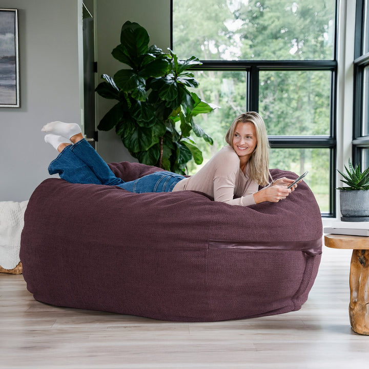 Woman lying on a large bean bag chair in a room with large windows and plants. #color_merlot-cloudweave