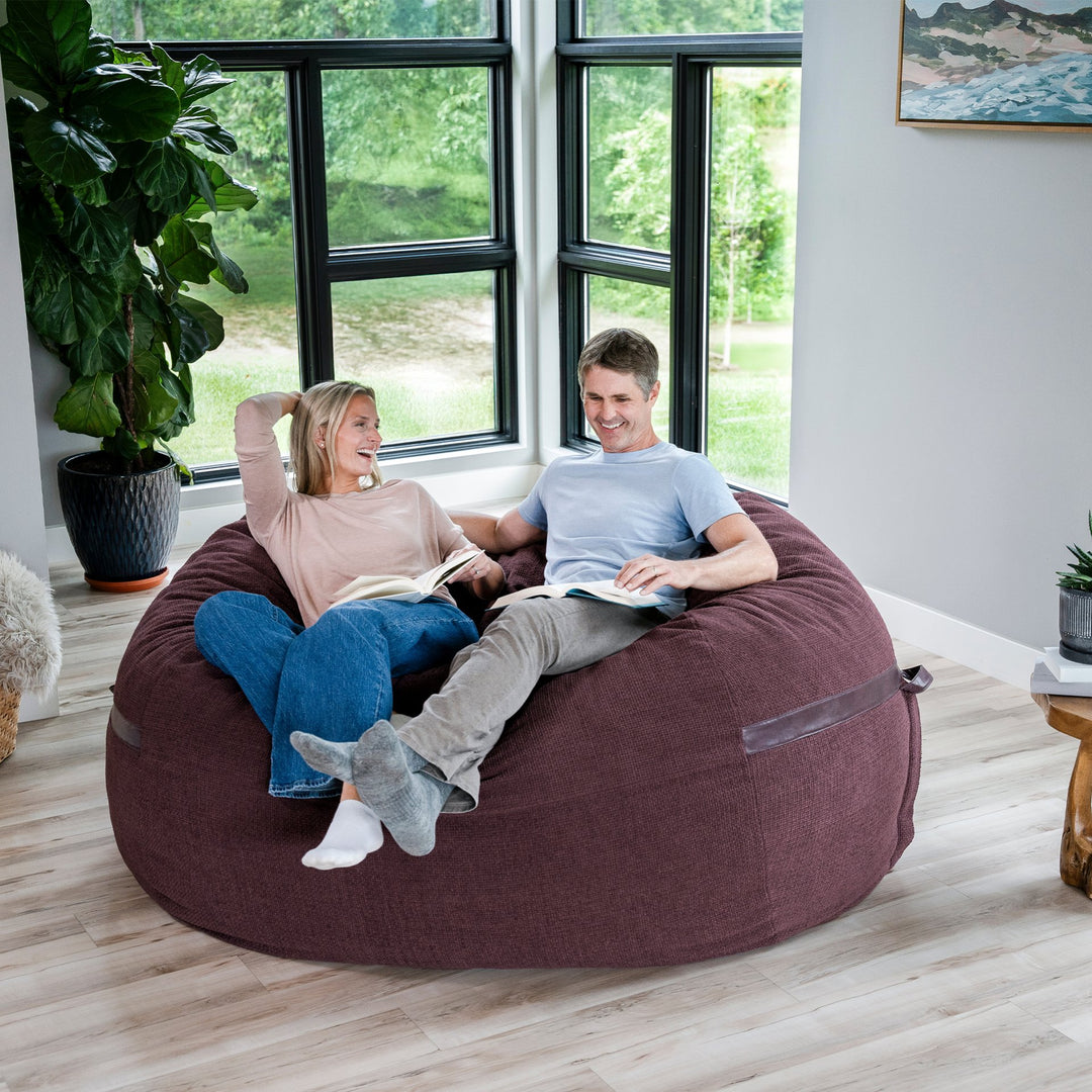 Two people sitting on a large bean bag in a room with large windows and plants. #color_merlot-cloudweave