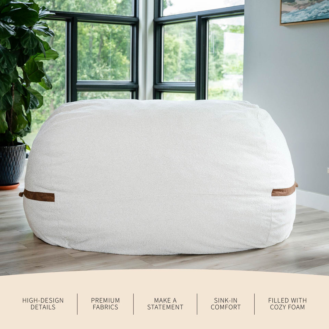 White bean bag chair with brown accents in a room with large windows and plants. #color_sandstone-textured-boucle