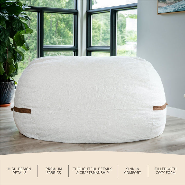 White bean bag chair with brown accents in a room with large windows and a plant. #color_sandstone-textured-boucle