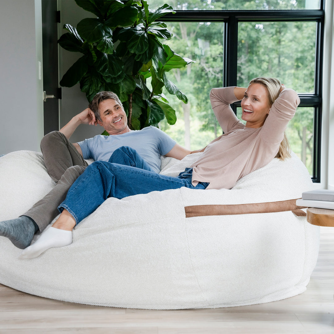 Man and woman relaxing on a large white bean bag chair in a modern living room. #color_sandstone-textured-boucle
