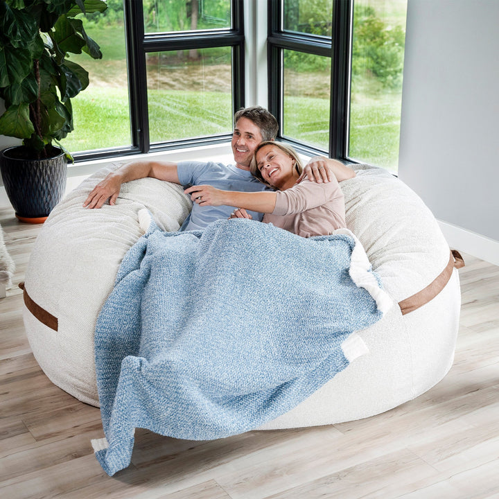 Couple relaxing on a large bean bag chair with a blue blanket in a bright room. #color_sandstone-textured-boucle