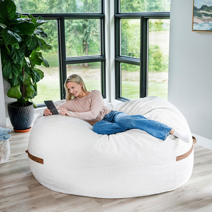 Woman sitting on a large white bean bag chair in a room with large windows and plants. #color_sandstone-textured-boucle