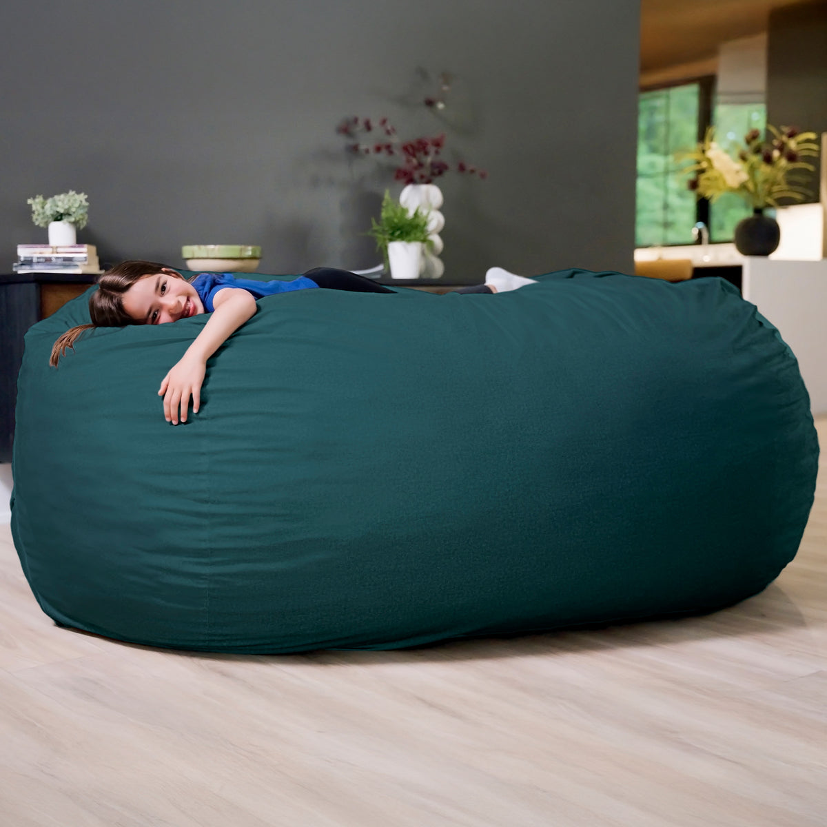 Person lying on a large teal bean bag in a room with plants and furniture. 