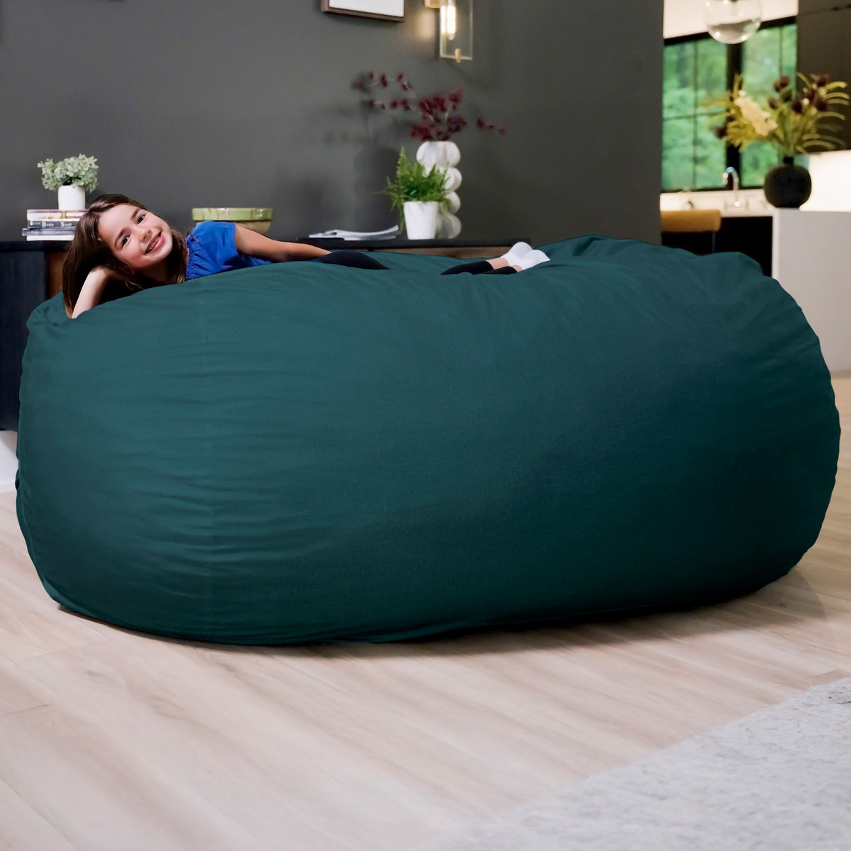 Large teal bean bag chair in a living room setting with a person lying inside. 