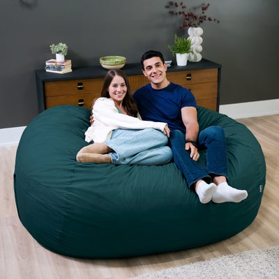Two people sitting on a large green bean bag chair in a room with a dresser and plants. 