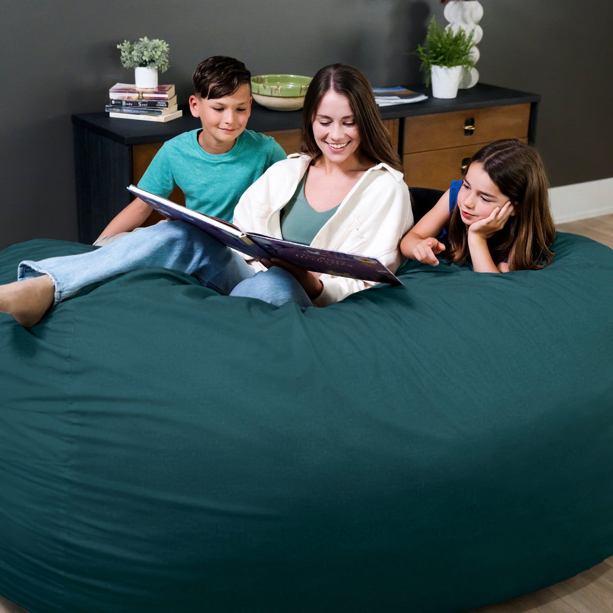 Woman reading a book to two children on a teal bean bag chair. 