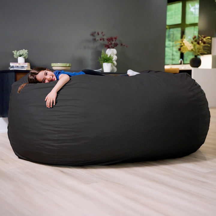 Person lying on a large black bean bag in a modern living room. #color_black-brushed-denim