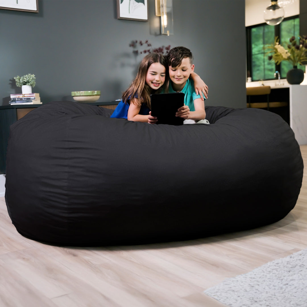Two children sitting on a large black bean bag in a living room. #color_black-brushed-denim