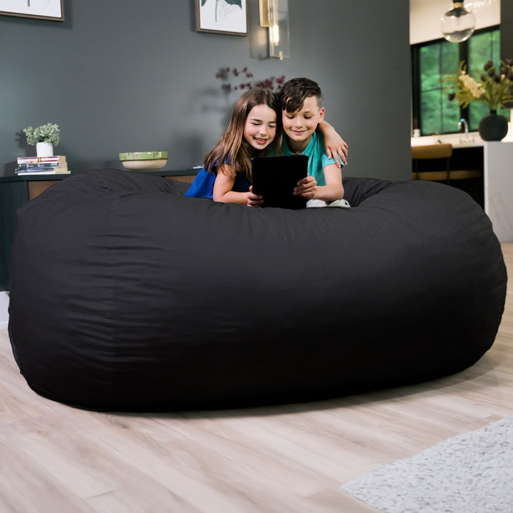 Two children sitting on a large black bean bag in a living room. #color_black-brushed-denim