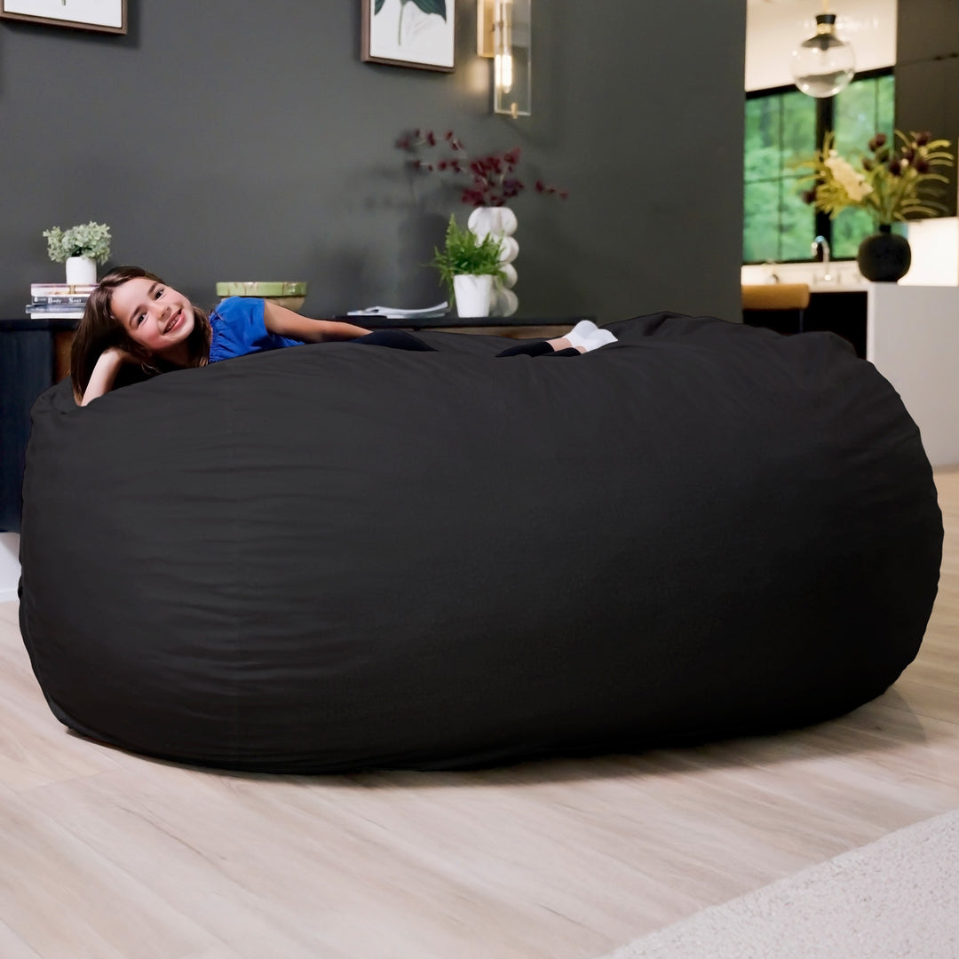 Large black bean bag chair in a room with a woman lying on it. #color_black-brushed-denim