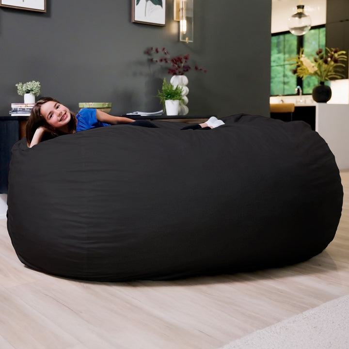 Large black bean bag chair in a room with a woman lying on it. #color_black-brushed-denim