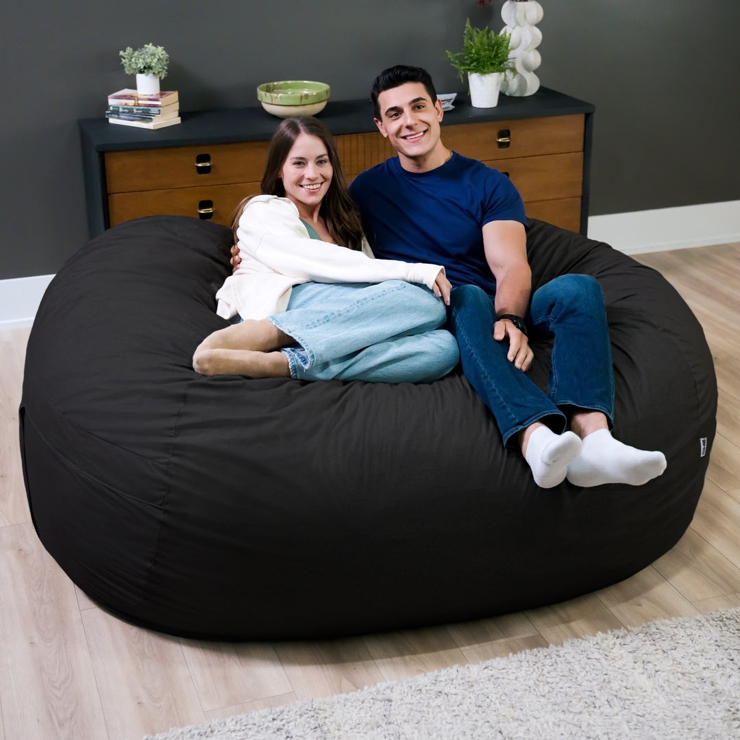 Two people sitting on a large black bean bag in a room with a dresser and decor. #color_black-brushed-denim