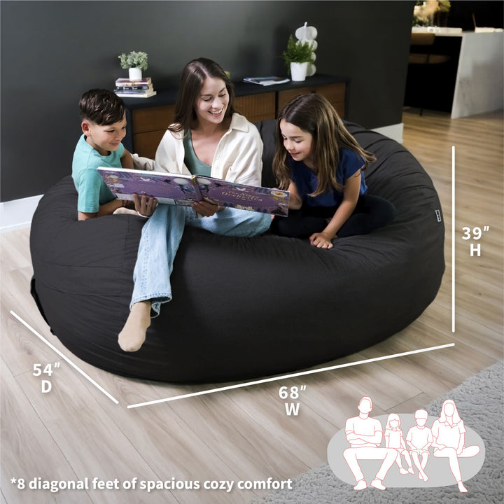 Woman reading a book to two children on a large black bean bag chair with measurements displayed. #color_black-brushed-denim