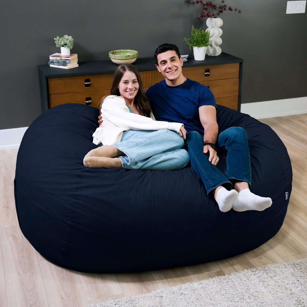 Two people sitting on a large navy bean bag in a room with a dresser and plants. #color_cobalt-brushed-denim
