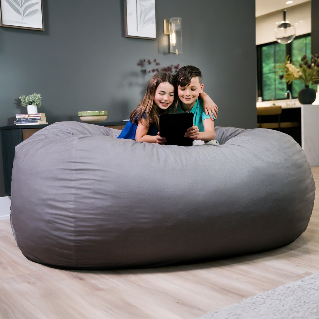 Two children sitting on a large gray bean bag in a living room. #color_fog-brushed-denim