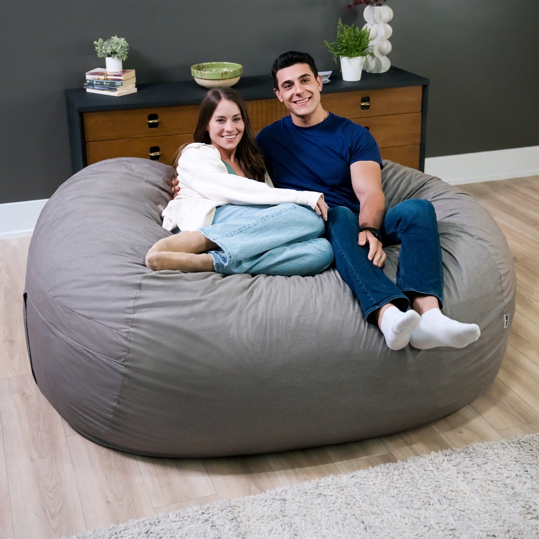 Two people sitting on a large gray bean bag chair in a room with a dresser and plants. #color_fog-brushed-denim