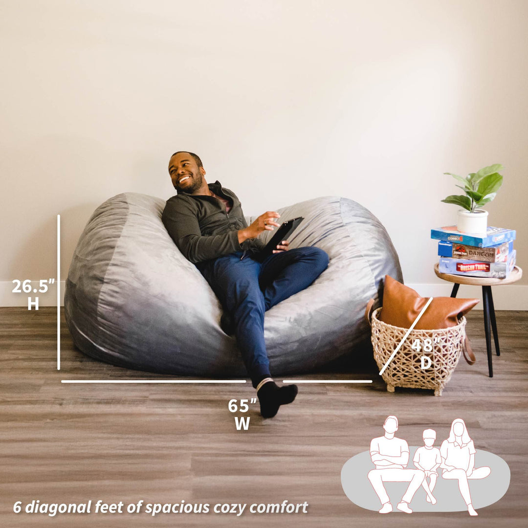 Man sitting on a large bean bag chair with measurements and comfort information displayed. #color_gray-plush
