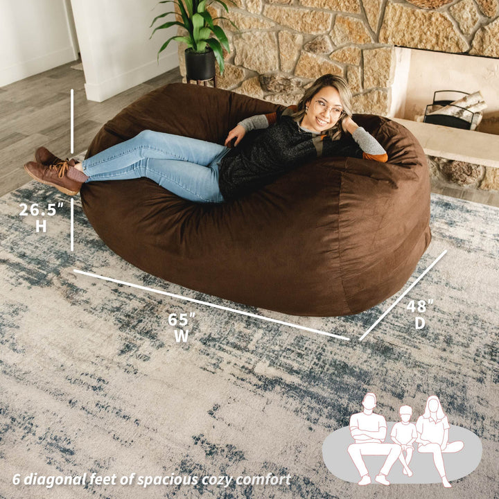 Woman sitting on a large brown bean bag chair with measurements and illustrations in a living room. #color_cocoa-brushed-denim