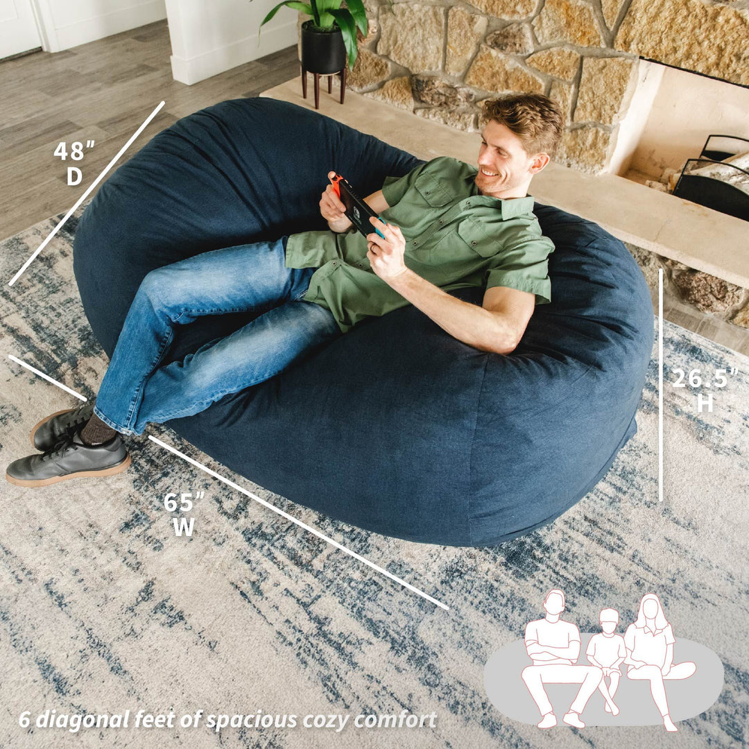 Man sitting on a large navy bean bag chair with measurements and illustrations of people sitting on it. #color_cobalt-brushed-denim