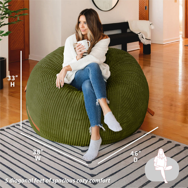 Woman sitting on a green bean bag chair with dimensions displayed #color_moss-green-corded-plush