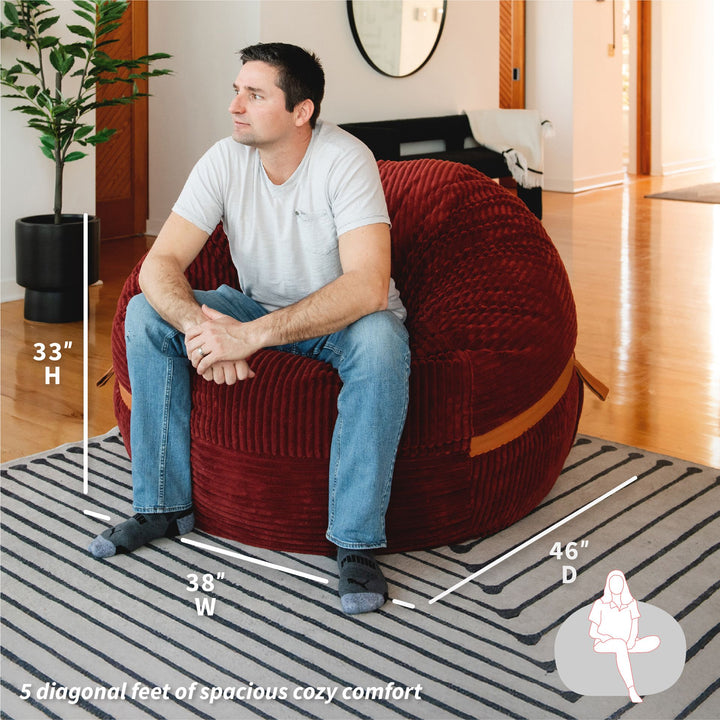 Man sitting on a red bean bag chair with measurements indicated #color_deep-terracotta-corded-plush