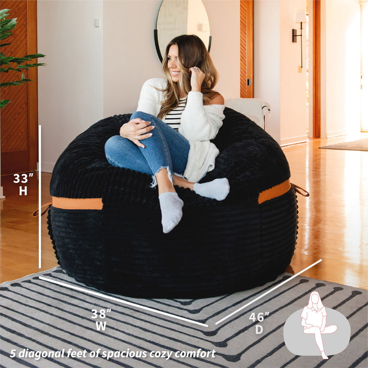 Woman sitting on a bean bag chair with dimensions displayed #color_black-licorice-corded-plush