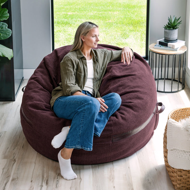 Woman sitting on a large maroon bean bag chair in a modern living room. #color_merlot-cloudweave