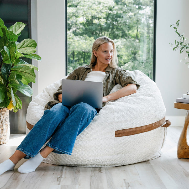 Woman using a laptop on a bean bag chair in a bright room with plants #color_sandstone-textured-boucle