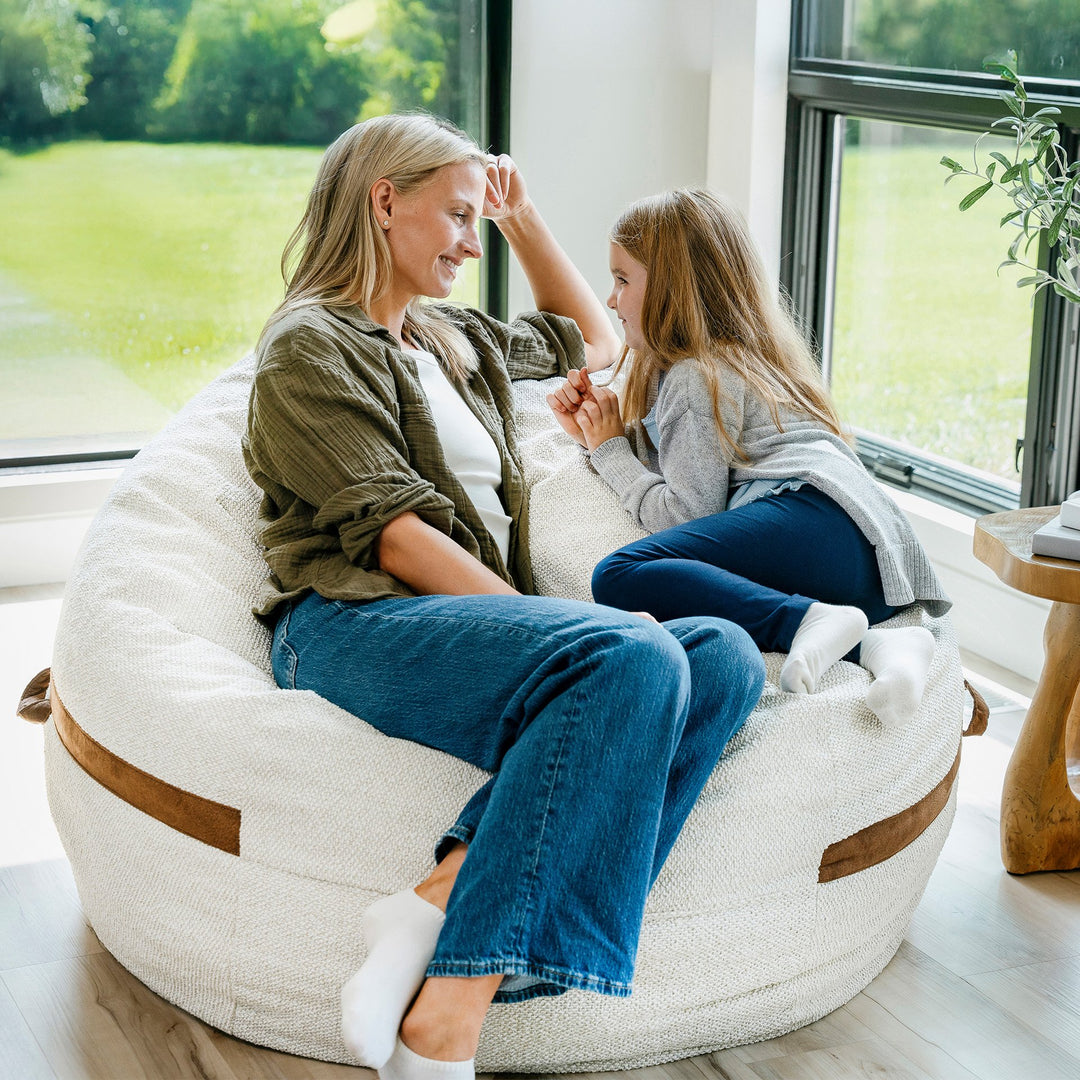 Woman and child sitting on a bean bag chair in a bright room with large windows. #color_sandstone-textured-boucle
