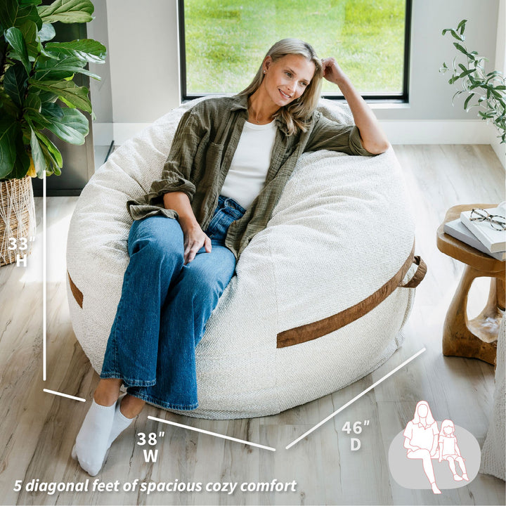 Woman sitting on a large white bean bag chair in a bright room with plants and a window. #color_sandstone-textured-boucle