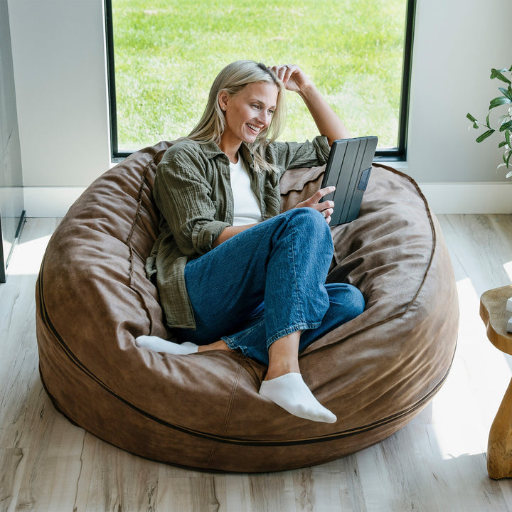 Woman using a laptop on a large brown bean bag chair in a bright room. #color_coffee-soft-vegan-leather