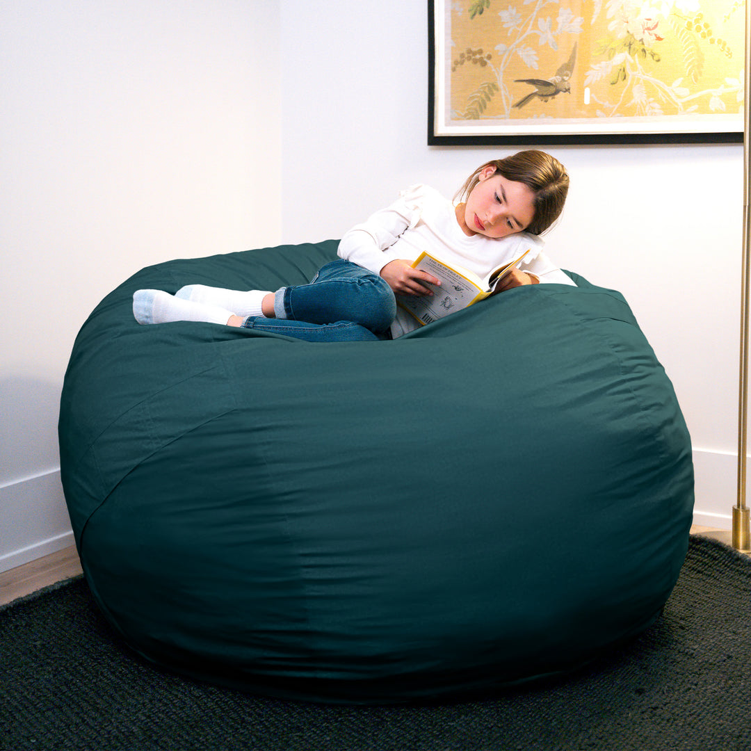 Child lying on a large green bean bag reading a book in a room with a painting on the wall. #color_deep-sea-velveteen