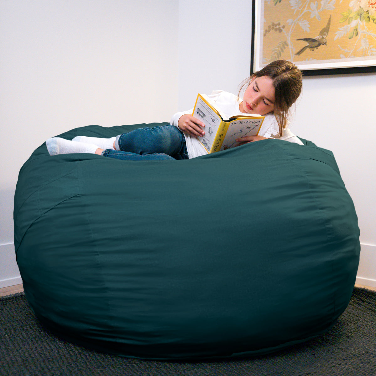Person reading a book on a large green bean bag chair in a room with a painting on the wall. 