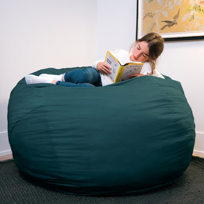Person reading a book on a large green bean bag chair in a room with a painting on the wall. 