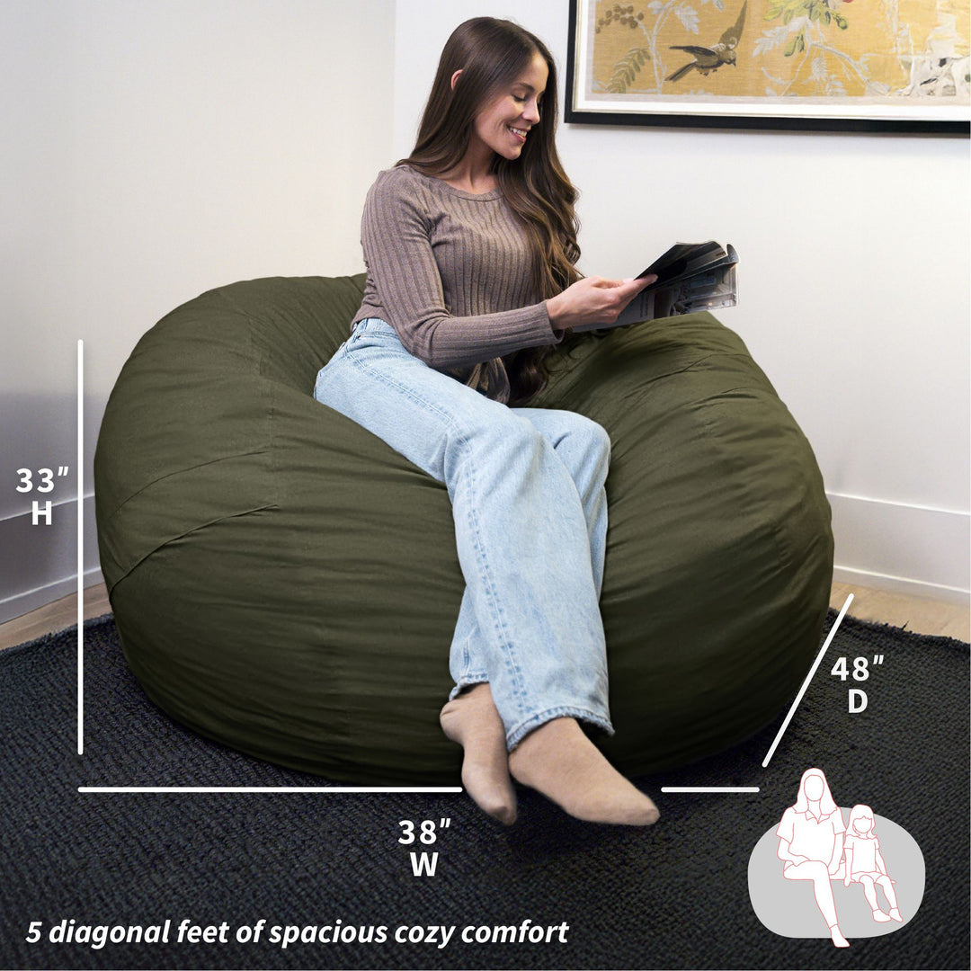 Woman sitting on a large green bean bag chair with measurements displayed. #color_forest-green-velveteen