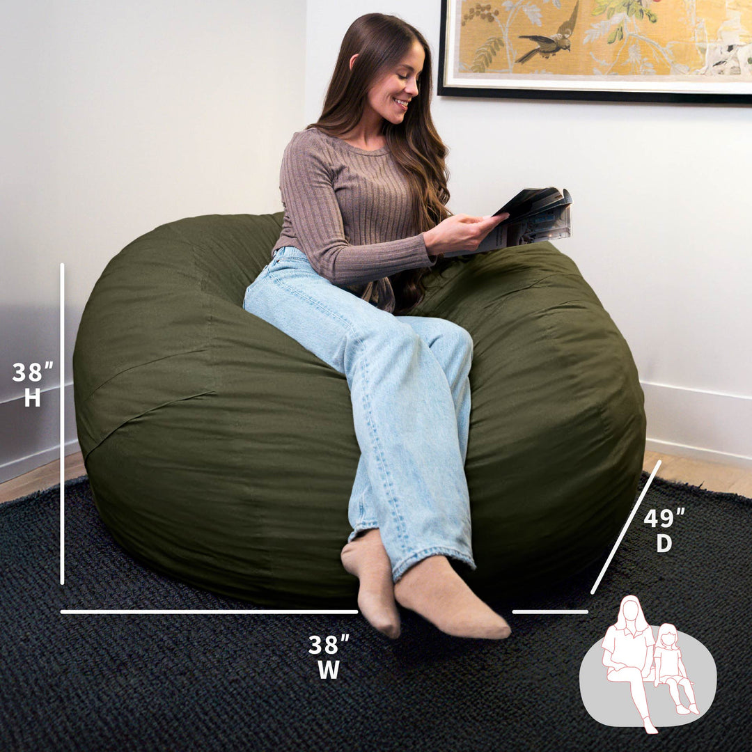 Woman sitting on a large green bean bag chair with measurements displayed. #color_forest-green-velveteen
