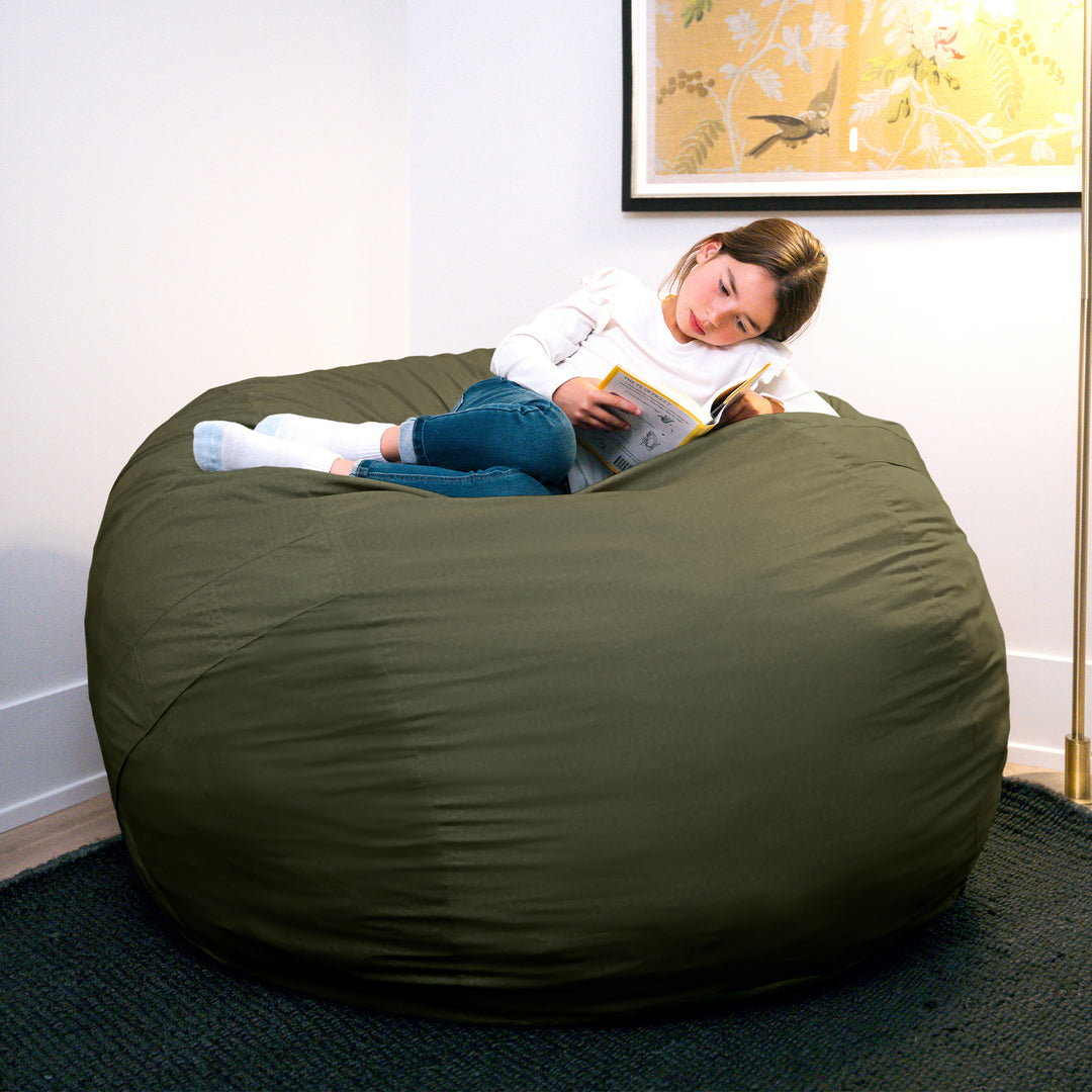 Child lying on a large green bean bag chair reading a book in a room with a painting on the wall. #color_forest-green-velveteen