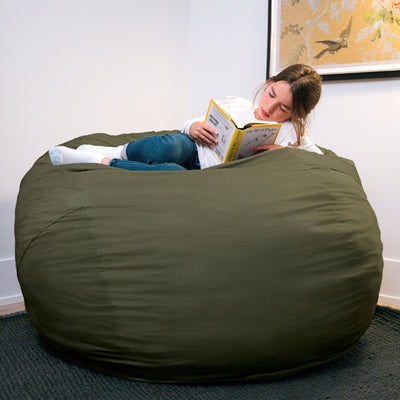 Person reading a book on a large green bean bag chair in a room with a white wall and framed picture. 