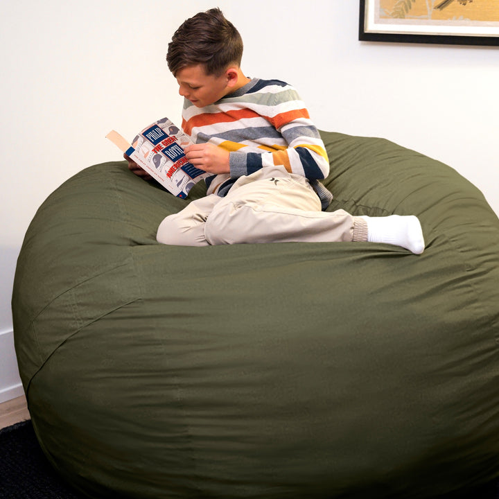 Person reading a book on a large green bean bag chair. #color_forest-green-velveteen