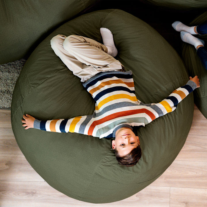 Child lying on a large green bean bag with striped shirt #color_forest-green-velveteen
