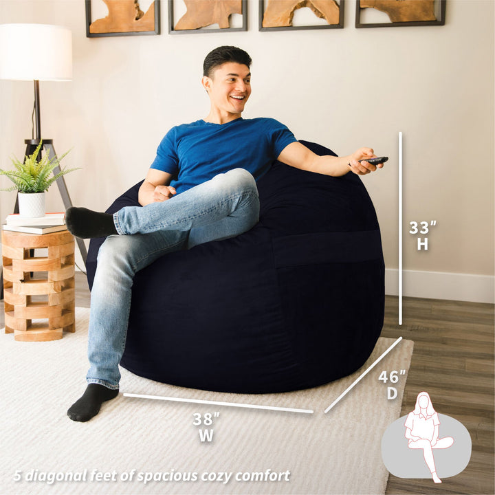 Man sitting on a black bean bag chair in a living room with dimensions displayed. #color_black-plush