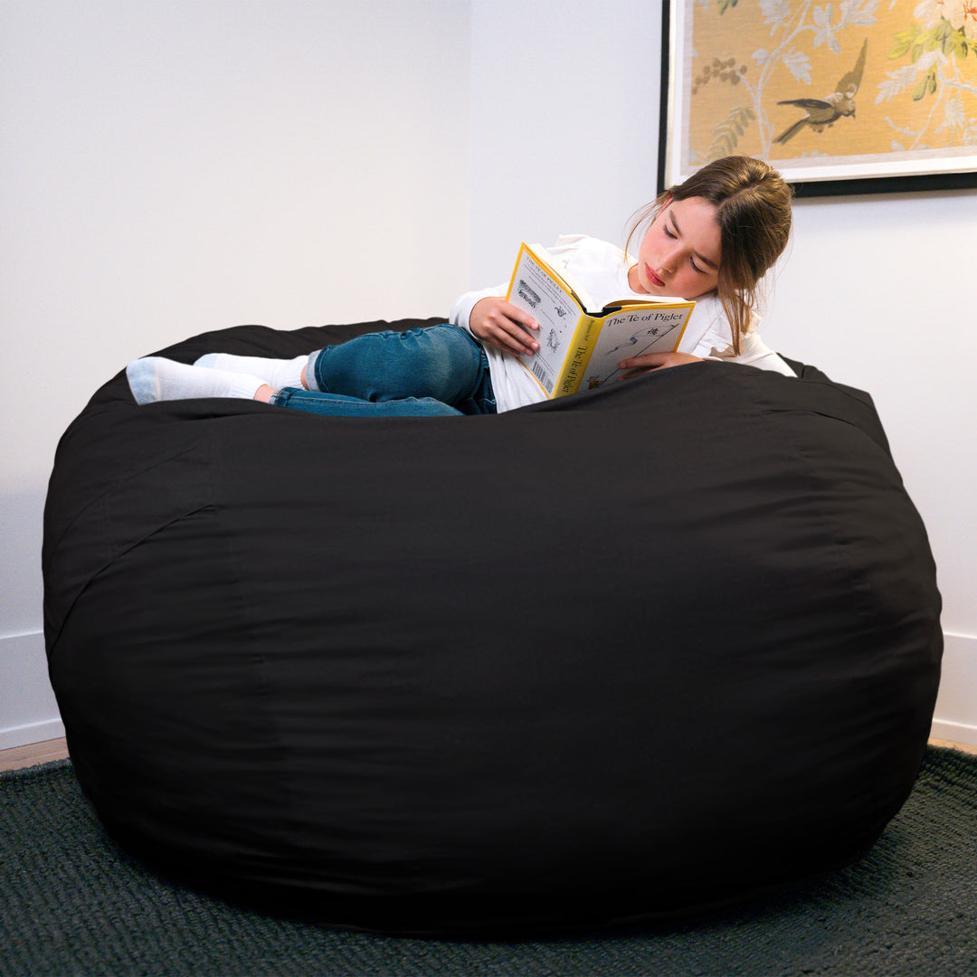 Person reading a book on a large black bean bag chair in a room with a painting on the wall. #color_black-brushed-denim