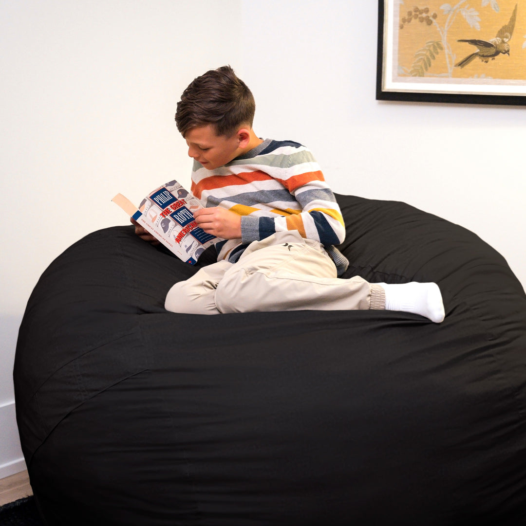 Person reading a book on a large black bean bag chair. #color_black-brushed-denim