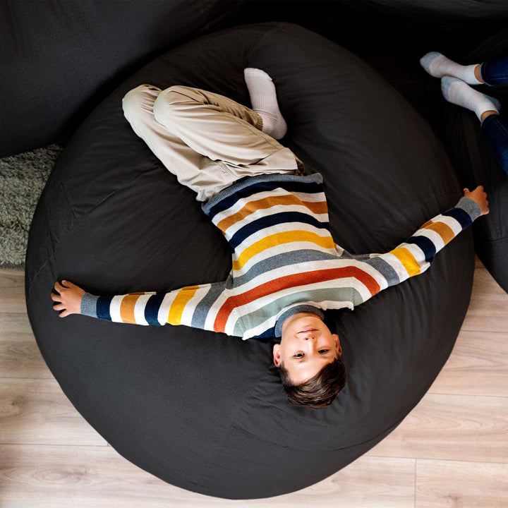 Child lying on a large black bean bag chair indoors #color_black-brushed-denim