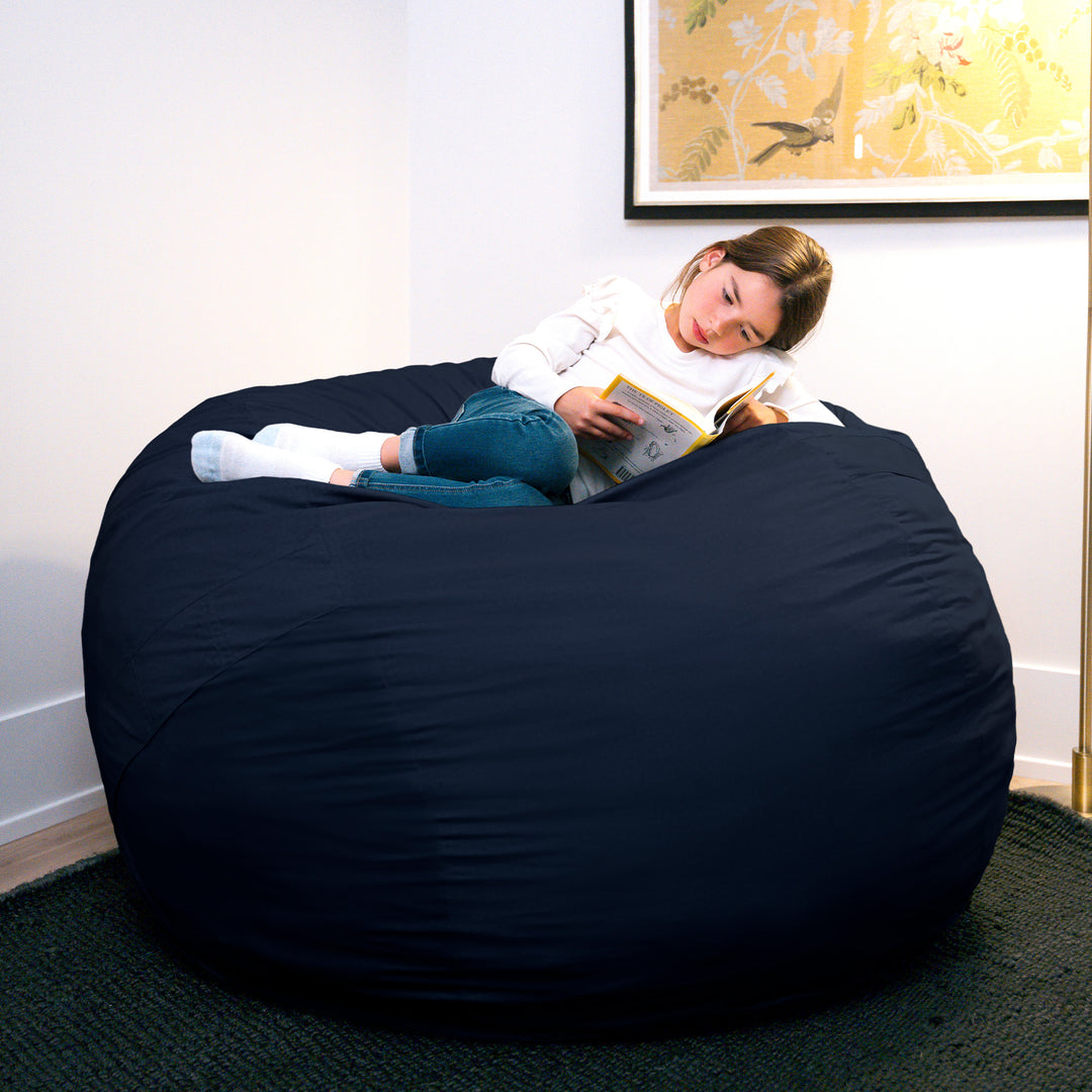 Person reading a book on a large navy bean bag chair in a room with a painting on the wall. #color_cobalt-brushed-denim